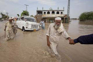 Elderly men wade past a stranded vehicle and a mosque while evacuating the flooded town of Nowshera