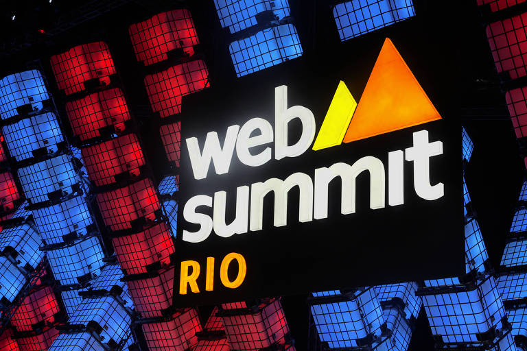 Palco decorado com colunas de neon azul e vermelho, e com letreiro branco e laranja com o nome do evento Web Summit Rio 
