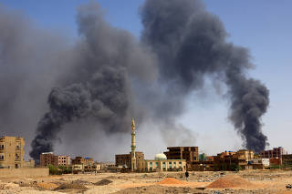 Man walks while smoke rises above buildings after aerial bombardment in Khartoum North