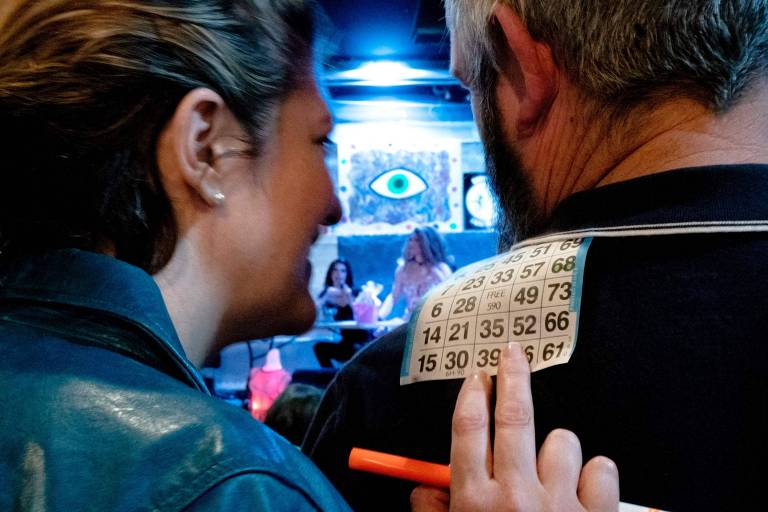 Mulher apoia papel de bingo nas costas de homem para marcar os números