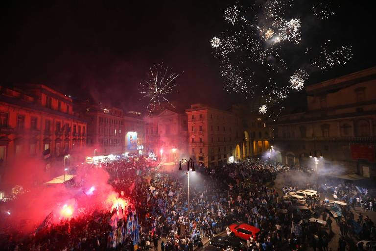 Multidão em praça observa queima de fogos de artifício no céu noturno 