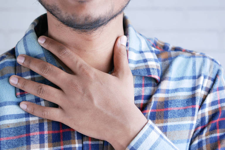 Imagem mostra homem de camisa xadrez e a mão sobre o pescoço, perto da laringe