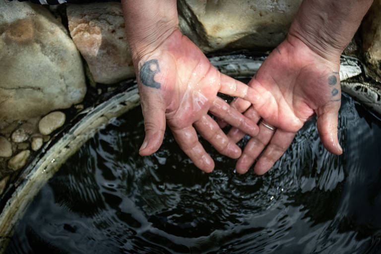 Foto mostra mãos de uma mulher branca com as palmas para cima acima de uma poça d'água