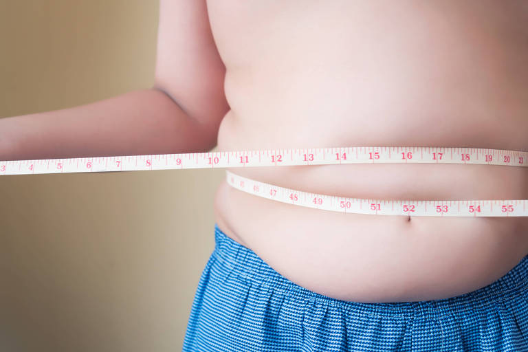 Menino com sobrepeso enrola fita métrica na barriga