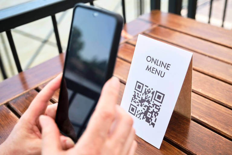 Mãos de uma mulher irreconhecível digitalizando um código QR com um smartphone para acessar o menu de um restaurante