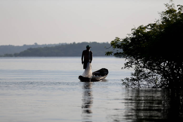 Pescador de pé contra o sol em uma pequena embarcação