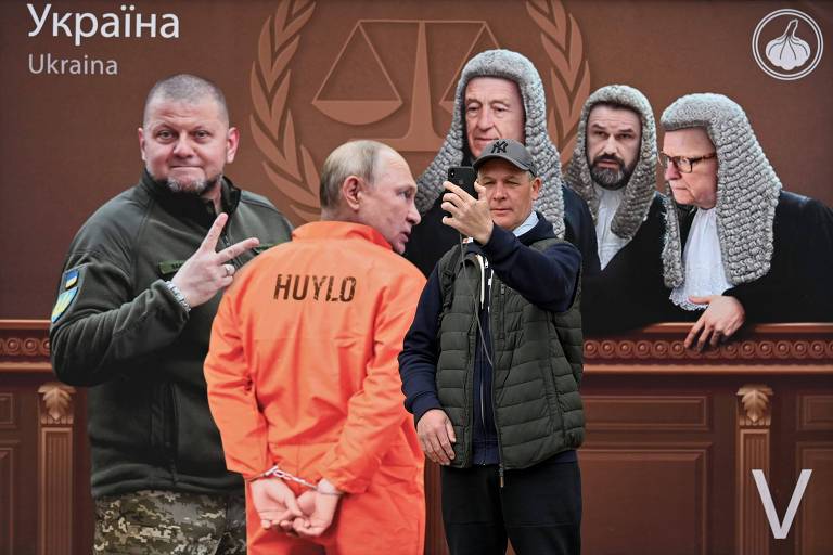 Em Kiev, homem tira selfie em frente a painel com ilustração de Vladimir Putin sendo preso após condenação no Tribunal de Haia, com Valerii Zaluzhnii, chefe das Forças Armadas da Ucrânia, comemorando