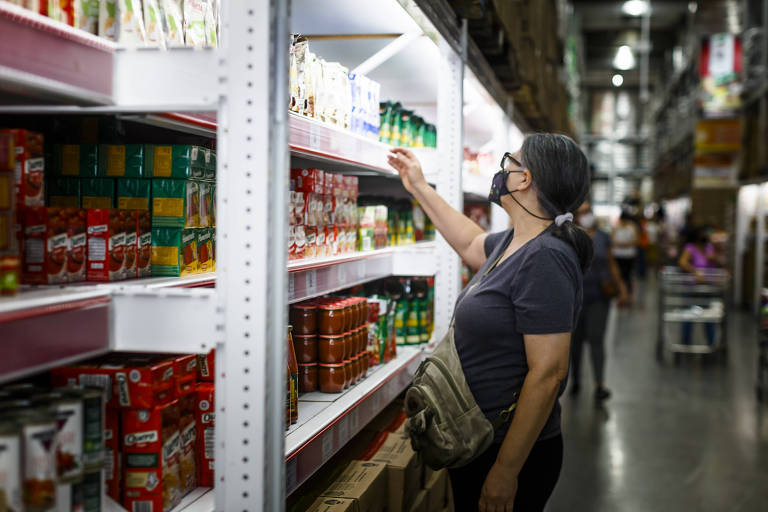Mulher pesquisa preços e olha produtos em gôndola de supermercado