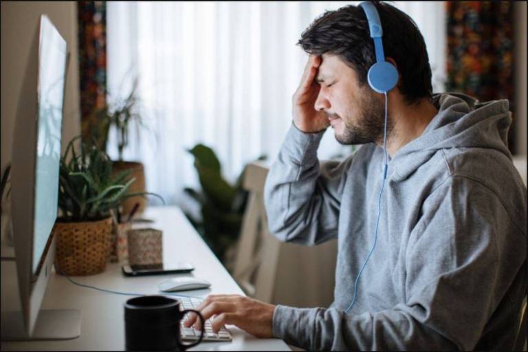 Homem de frente para uma tela de computador e com fone de ouvido coloca uma mão no rosto simbolizando desapontamento