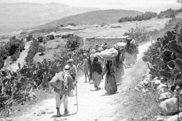 Foto em preto e branco mostra pessoas caminhando com seus pertences em meio a paisagem com cactos