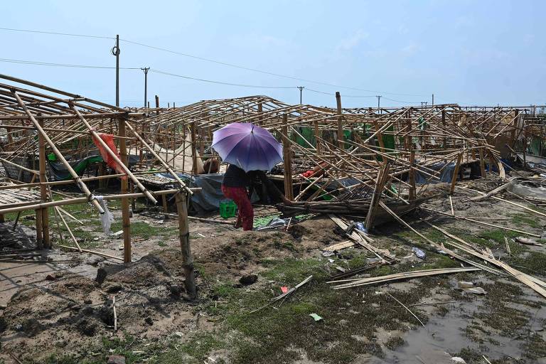 Mulher com guarda-chuva enquanto tenta limpar destroços após passagem do ciclone Mocha pelo campo de refugiados Pyone Yay, no nordeste de Mianmar