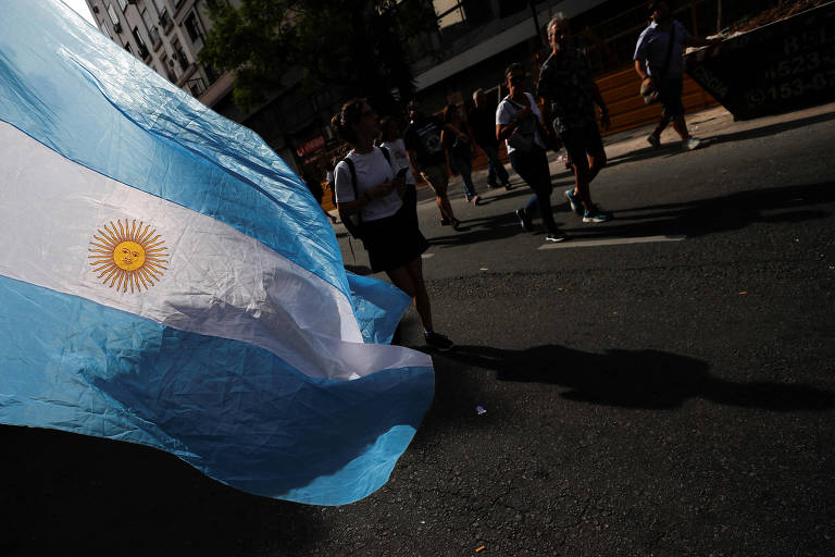 Pessoas caminham em rua de Buenos Aires em data para marcar 47 anos do golpe militar na Argentina, com bandeira do país flamulando à esquerda da imagem