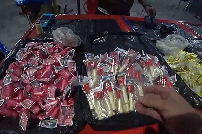 Imagem mostra pinos de cocaína e outros tipos de droga em cima de uma mesa vermelha para serem vendidos