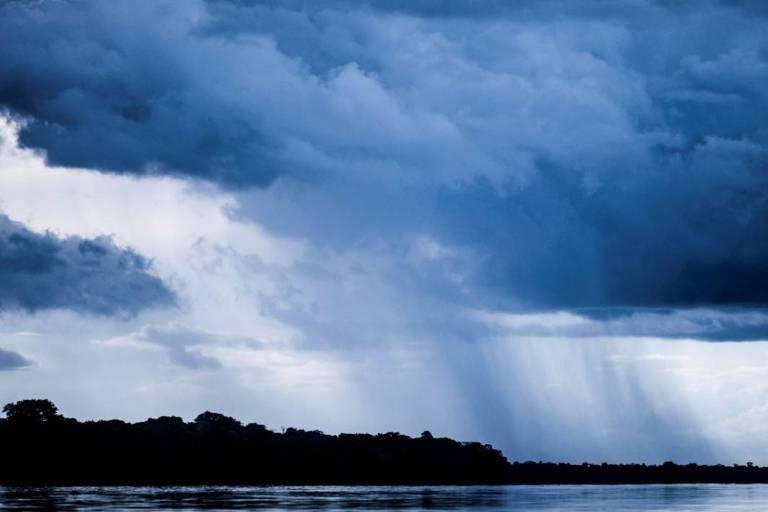 Nuvens carregadas e chuva forte sobre uma floresta e um rio na Amazônia