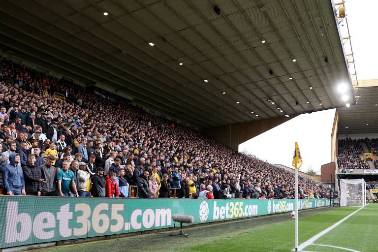 Placa de publicidade no estádio Molineux exibe marca de casa de apostas durante partida da Premier League