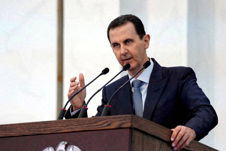 Retrato de Assad em um plenário, falando ao microfone