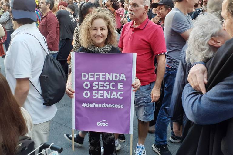 Em foto colorida, a cantora Anaí Rosa segura um cartaz com os dizeres Defenda o Sesc e o Senac