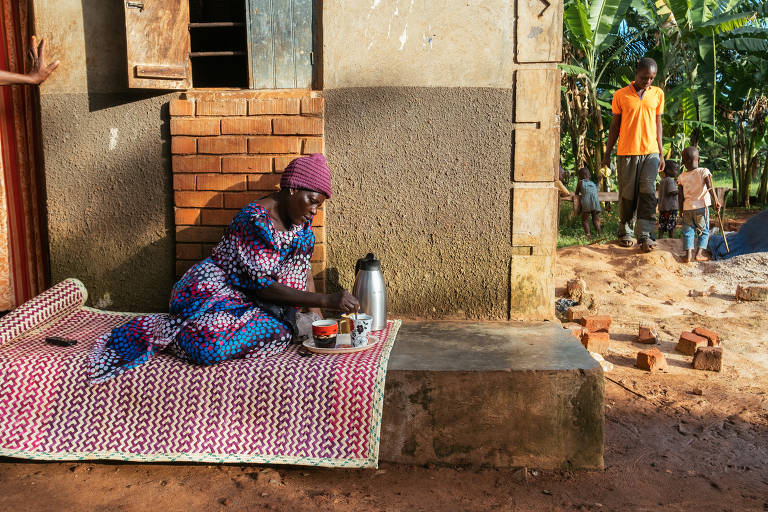 Sentada em um tapete na varanda de sua casa, Margaret Nasamba prepara café em sua casa em Zirobwe, Uganda