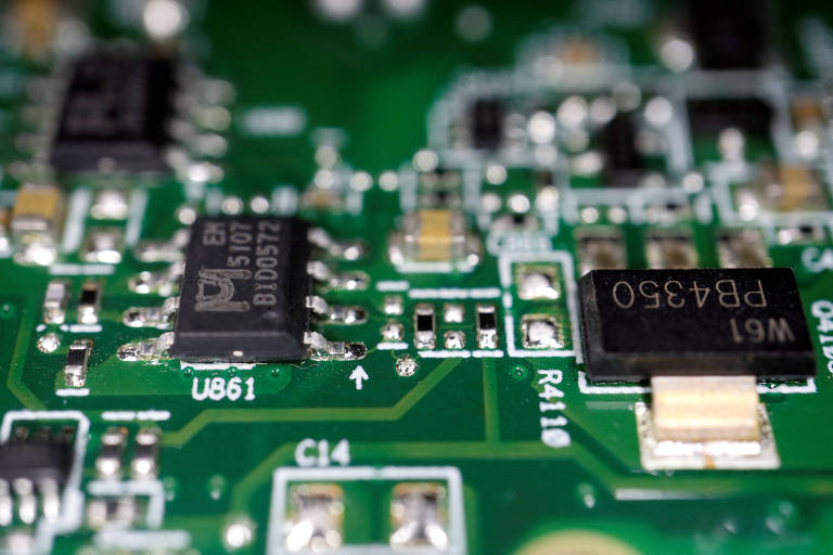 Chips fabricados na China são vistos em placa de computador. A Placa é verde, com detalhes em solda prateados e chips pretos.