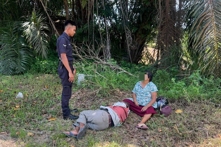 Um policial conversa com um casal no chão, que quase desmaiou devido ao calor em Segamat, na Malásia