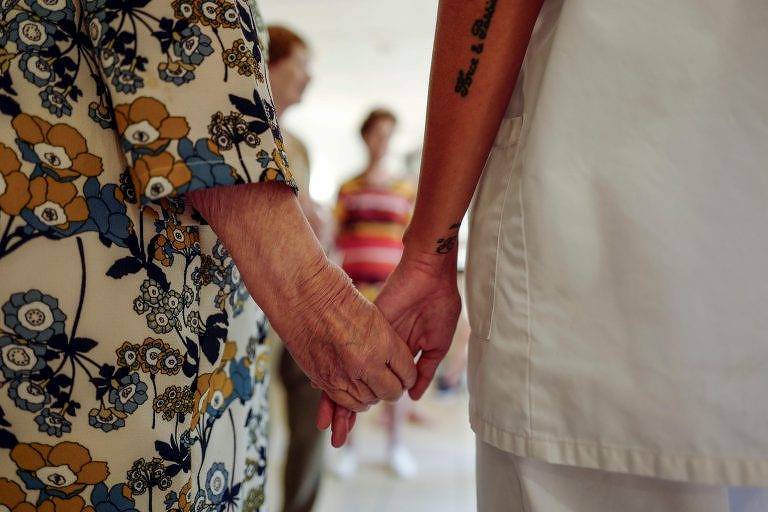 Terapeuta segura a mão de paciente idosa, na França (Valery Hache/AFP)