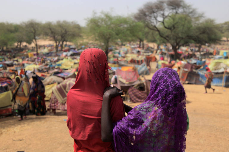 Mulheres olham para abrigos improvisados a deslocados de conflito na fronteira do Sudão com o Chade