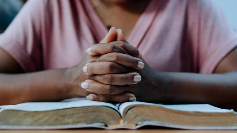 Criança não identificada com as mãos unidas em oração sobre um livro