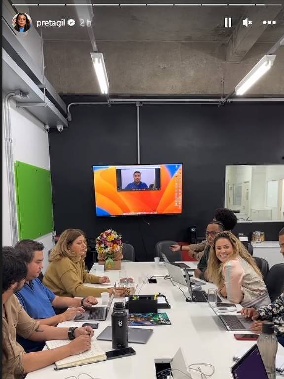 Em foto colorida, um grupo de pessoas aparecem sentados em uma mesa para reunião de trabalho