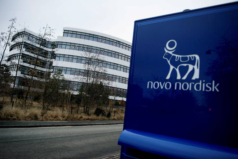 Logo da Novo Nordisk em placa azul e, ao fundo, separado por uma estrada, um edifício  