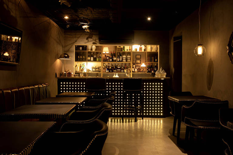 Ambiente do restaurante  Punk Cuisine, em São Paulo; salão está à meia luz, escuro, com um balcão de drinques iluminado ao fundo