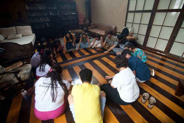 Grupo de pessoas está sentada no chão fazendo um círculo em um tipo de dinâmica interativa