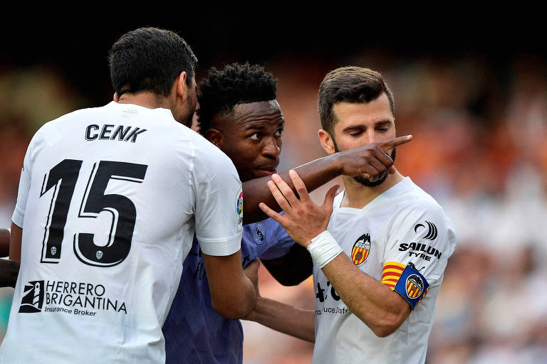 Entre dois jogadores do time adversário, Vinicius Junior, do Real Madrid, aponta para o local no estádio Mestalla onde torcedores do Valencia desferiram ataques racistas a ele em jogo do Campeonato Espanhol