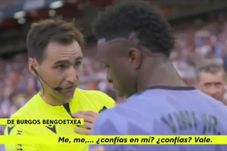 Imagem colorida mostra o árbitro espanhol conversando frente a frente com Vinicius Junior. Vinicius está cabisbaixo, e o árbitro tenta olhar em seus olhos enquanto pede confiança