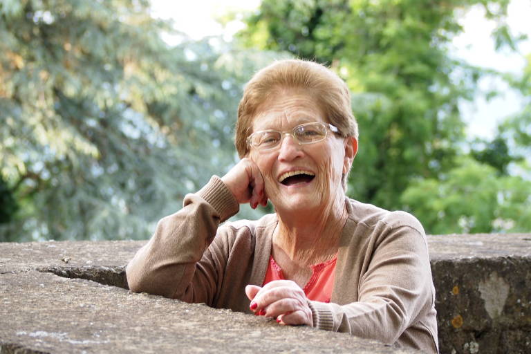 Uma senhora sorridente apoiada no parapeito da varanda de casa