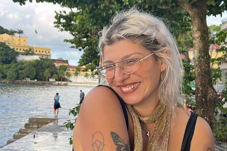 A influenciadora portuguesa Layla Zamorano sorri para foto enquanto segura celular; ela é uma mulher branca com cabelos platinados