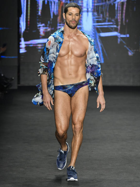 José Loreto, usando uma sunga azul cavada e uma camisa azul florida, sem camiseta sob esta peça, desfilando para a The Paradise na São Paulo Fashion Week