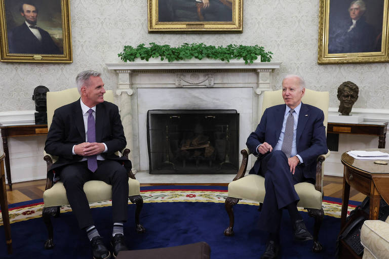 dois homens brancos de terno sentados, com uma lareira por trás 