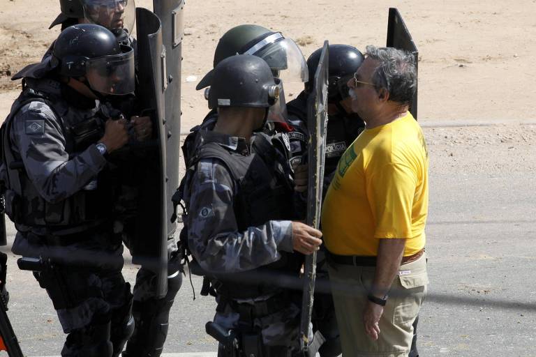 Homem de verde amarelo diante de policiais com uniforme preto e escudo
