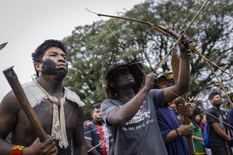 Indígenas protestam contra o março temporal, segurando pedaços de pau e arco e flecha