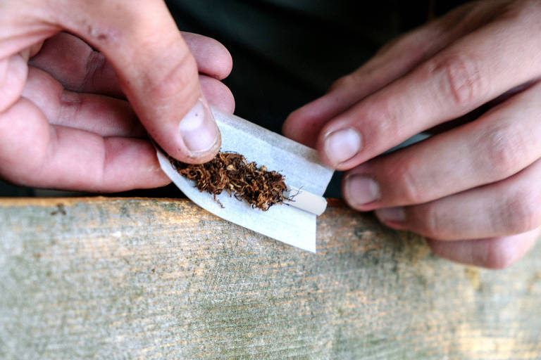 a person rolls a cigarette with tobacco