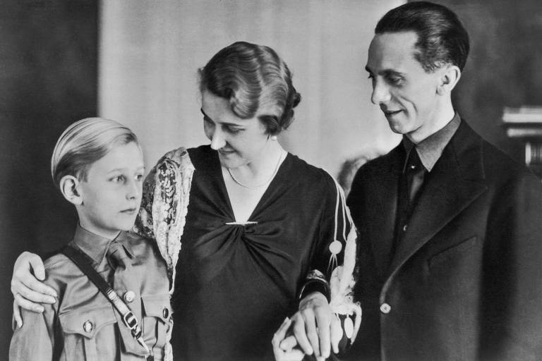criança vestindo uniforme nazista ao lado de dois adultos