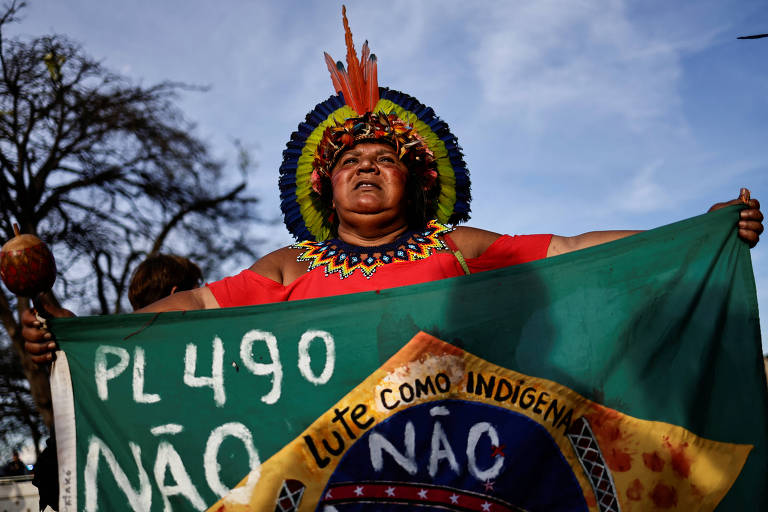 Com uma bandeira do Brasil com a frase PL 490 Não, indígena Pataxó protesta contra a votação do marco temporal em Brasília