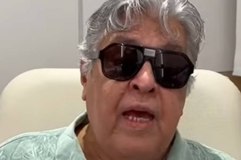 Em foto colorida, homem de óculos escuros faz um vídeo do quarto de um hospital