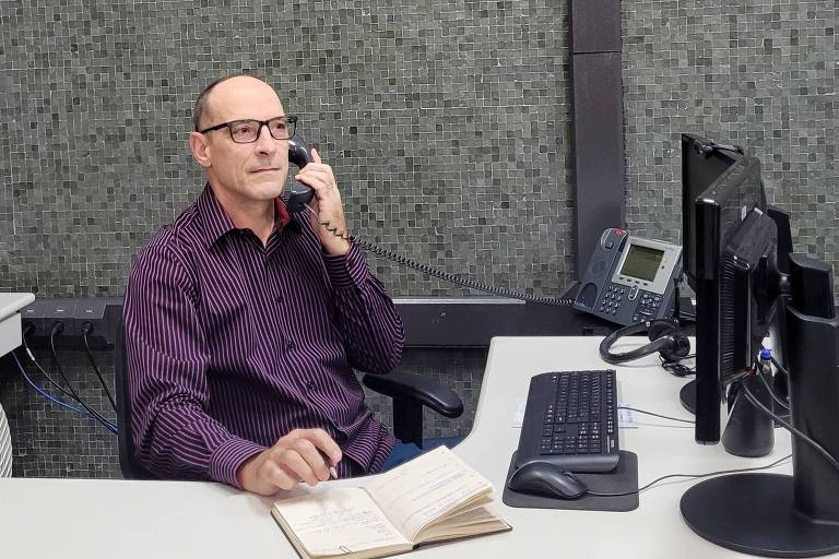 A imagem mostra um homem de óculos falando ao telefone