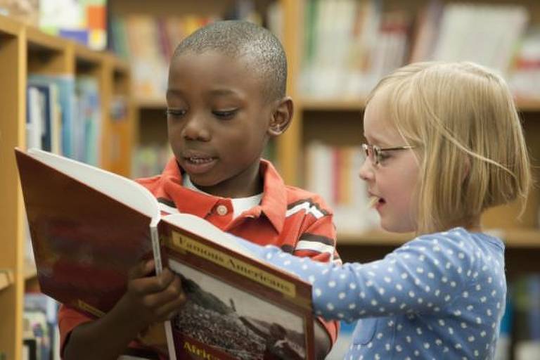 Crianças leem livro em biblioteca