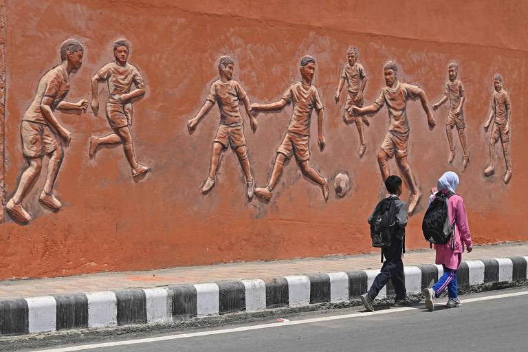Crianças em idade escolar caminham com mochilas perto de mural em Srinagar, na Índia