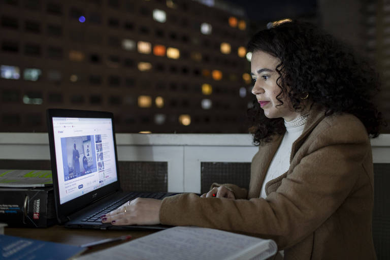 Imagem colorida mostra Lígia, uma mulher branca de 31 anos, sentada e olhando para a tela de um computador