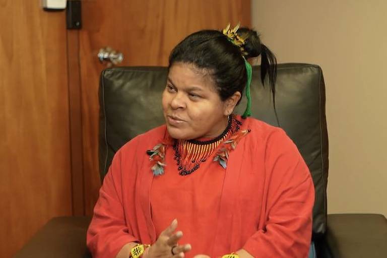 Ministra dos Povos Indígenas, Sônia Guajajara veste blusa vermelha e está sentada em poltrona