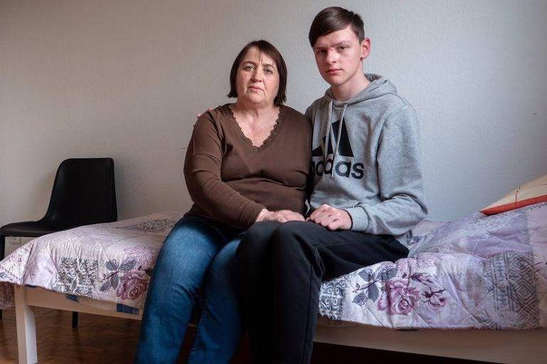 Tetiana Krainiuk e seu filho Sasha estão sentados em uma cama olhando para a câmera