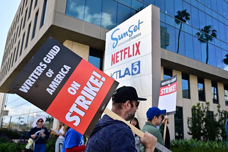 Roteirista com placa de greve anda carregando placa em frente a estúdio da Netflix